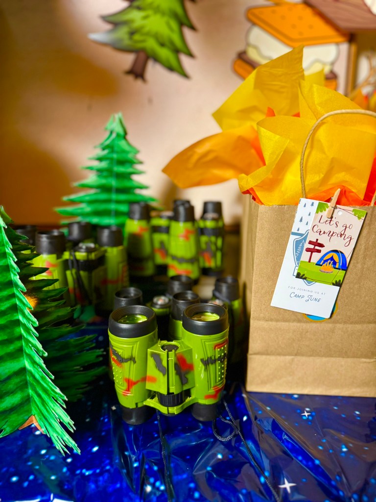 Kids camping party favors with binoculars, canteens, goodie bags, and woodland table decor.