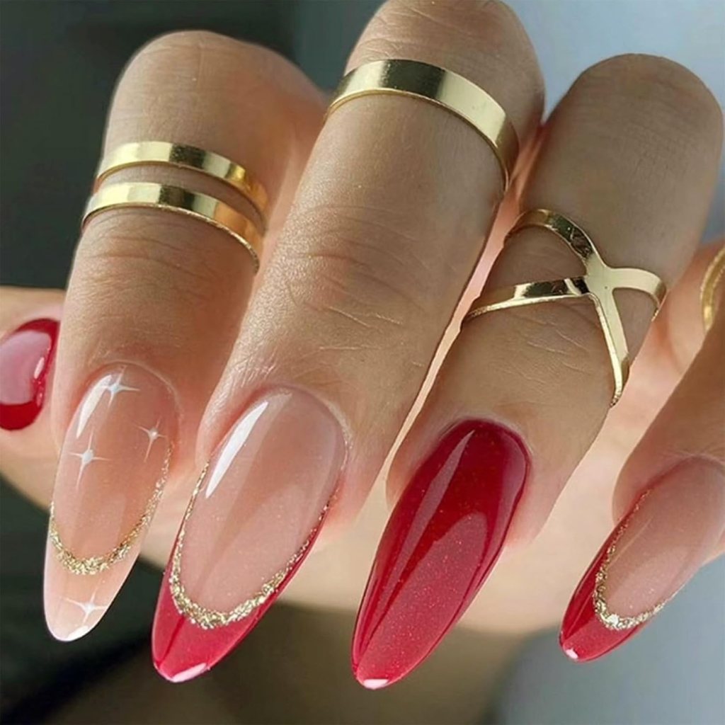 Close-up of a hand showcasing long, stylish nails painted with a combination of red and nude polish, featuring gold accents and rings on the fingers.