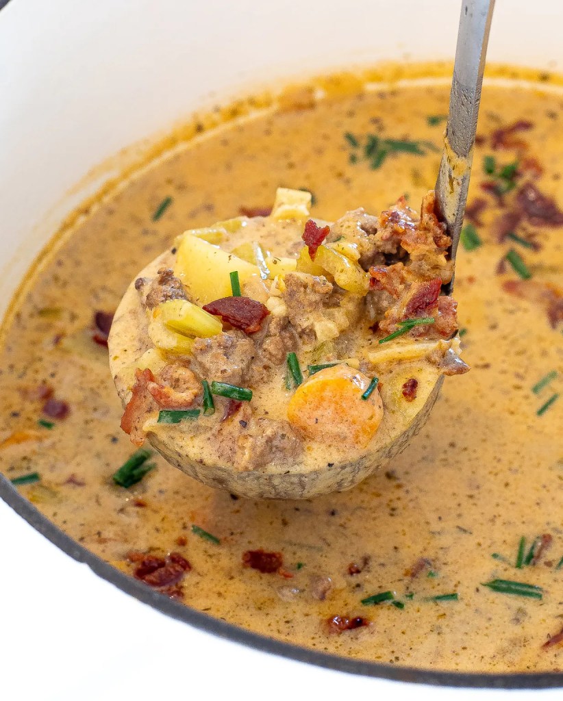 A close-up of a ladle serving creamy soup filled with vegetables and meat, showcasing a hearty, comforting dish.