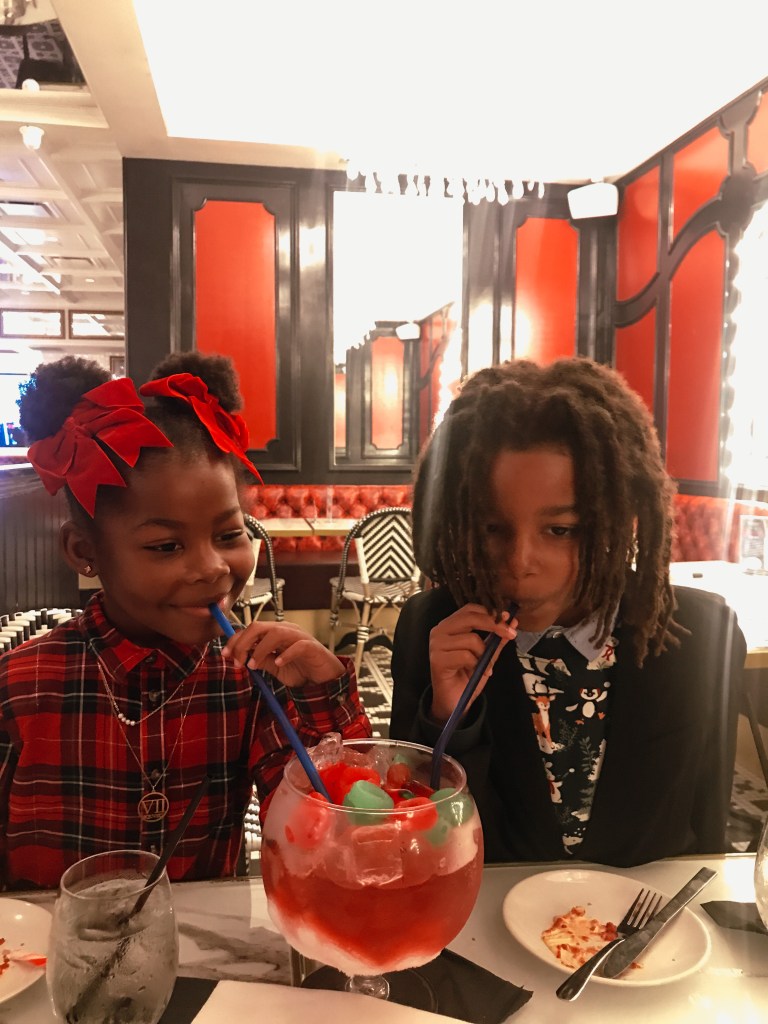 Two children enjoying a colorful non-alcoholic signature goblet at Sugar Factory Biloxi during a family Christmas visit.