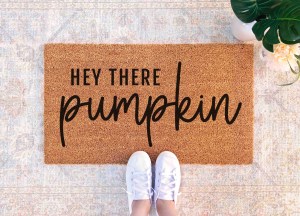 A cozy doormat with the text 'HEY THERE PUMPKIN' in a playful font, surrounded by a neutral-toned setting.