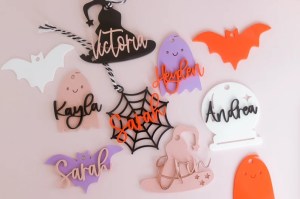 Colorful Halloween name tags featuring ghosts, bats, and a witch hat, personalized with different names, displayed on a pink background.