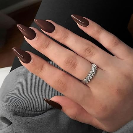 Close-up of elegantly manicured almond-shaped nails painted in a rich chocolate brown color, wearing a sparkling silver ring against a cozy knit sweater.