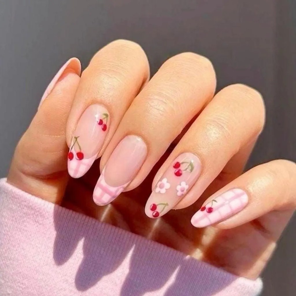 A hand displaying a stylish manicure featuring light pink nail polish with cherry and flower designs on the nails.