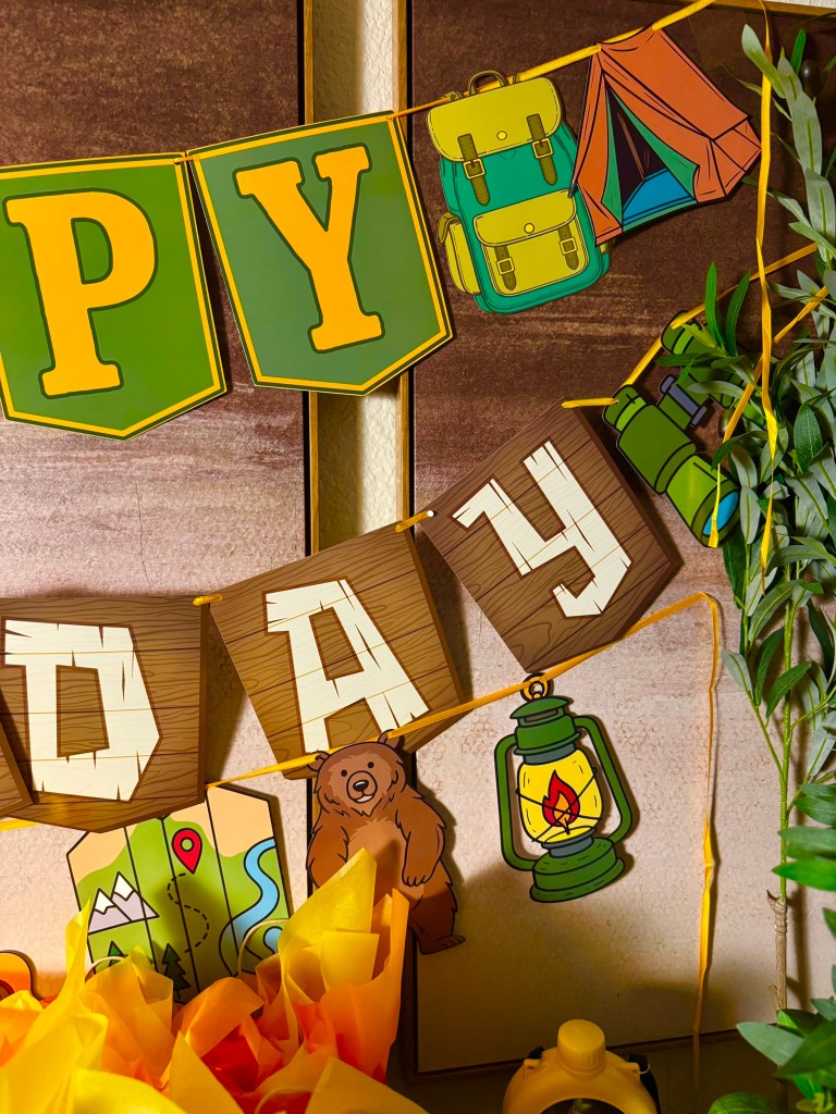 Rustic camping birthday banner with wood-style letters and woodland party decorations.