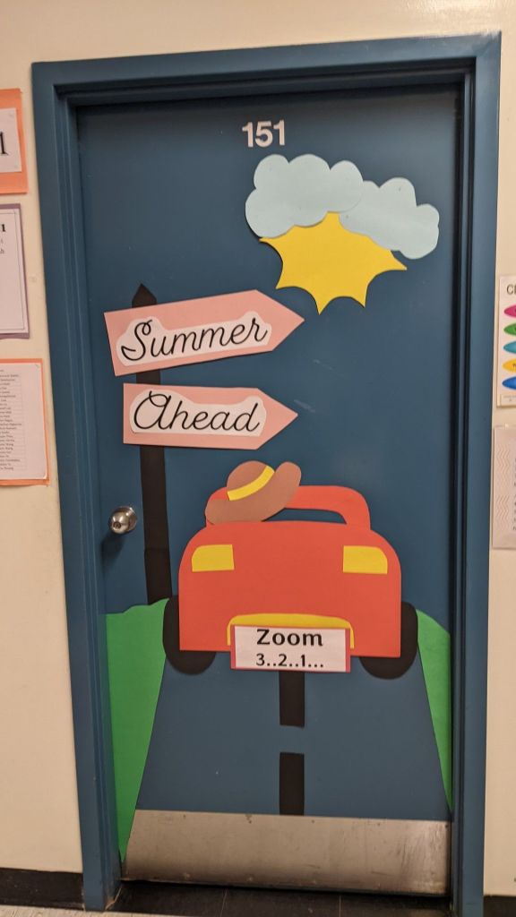 Decorated classroom door with a summer theme featuring a red car, clouds, sun, and signs that read 'Summer Ahead' and 'Zoom 3...2...1...'
