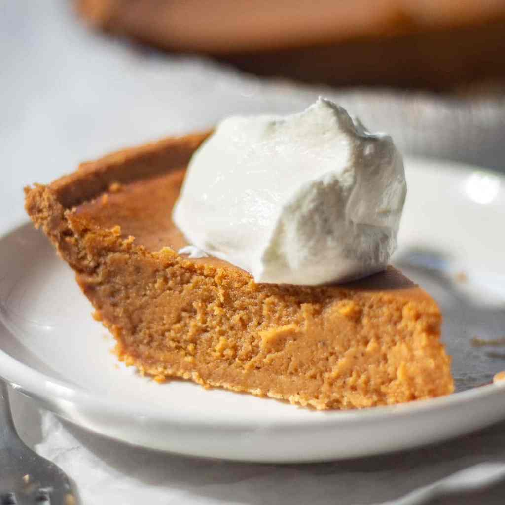 A slice of pumpkin pie topped with a dollop of whipped cream on a white plate.