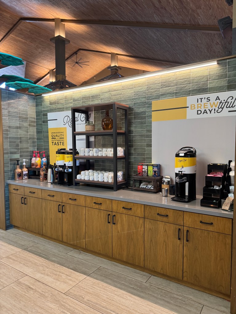 A coffee area at Great Wolf Lodge in Grapevine, TX featuring a modern setup with various coffee dispensers, condiments, and decorative signage that promotes quality beverages.