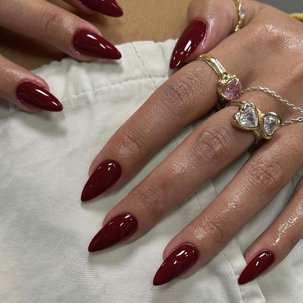 Close-up of hands with long, pointed red nails, adorned with several gold rings on fingers.