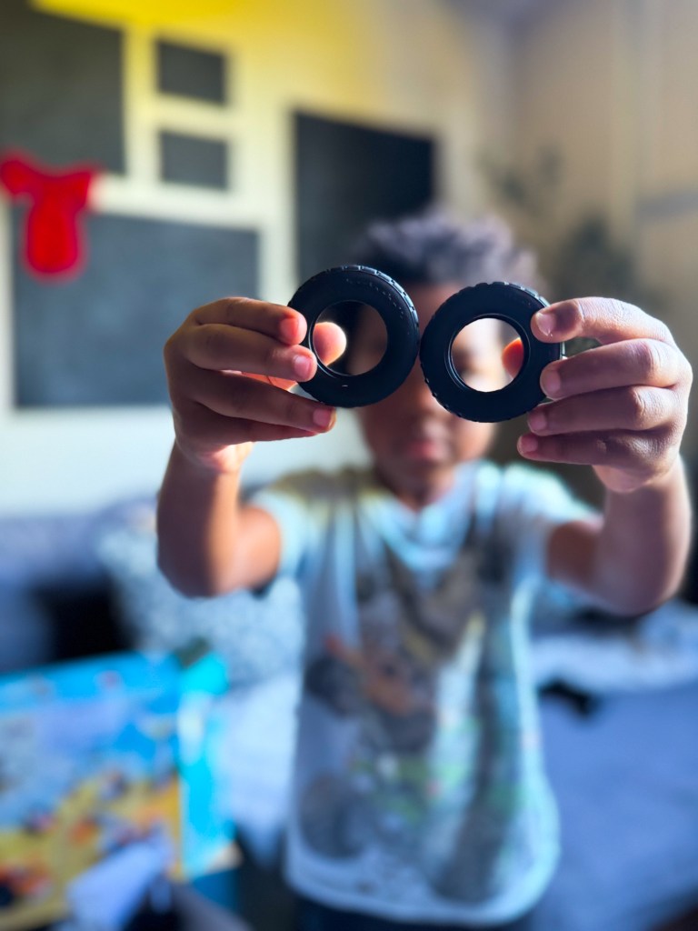 A child holding two black toy tires in front of them, with a blurred living room background.