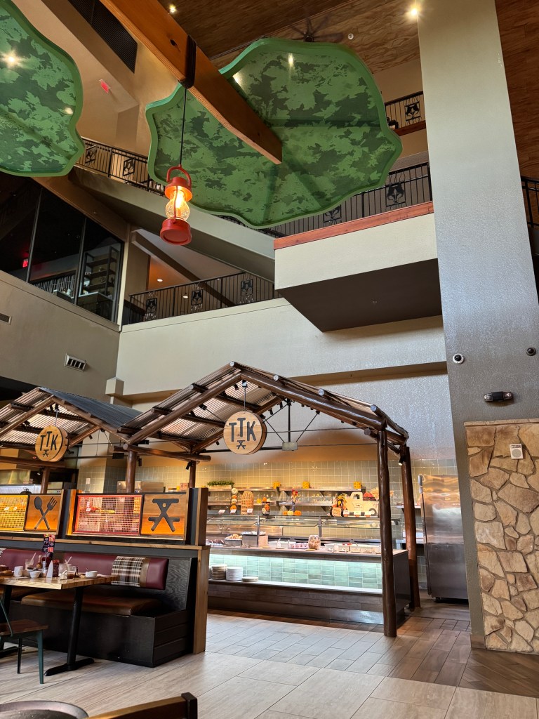 Interior view of Great Wolf Lodge dining area with a rustic design, featuring wooden beams, greenery overhead, and food display counters.