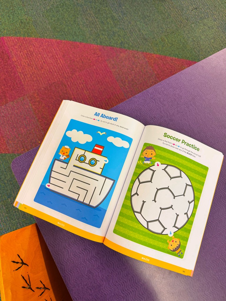 An open children's activity book featuring two maze games: one depicting a ship and the other a soccer ball, with colorful illustrations and instructions.