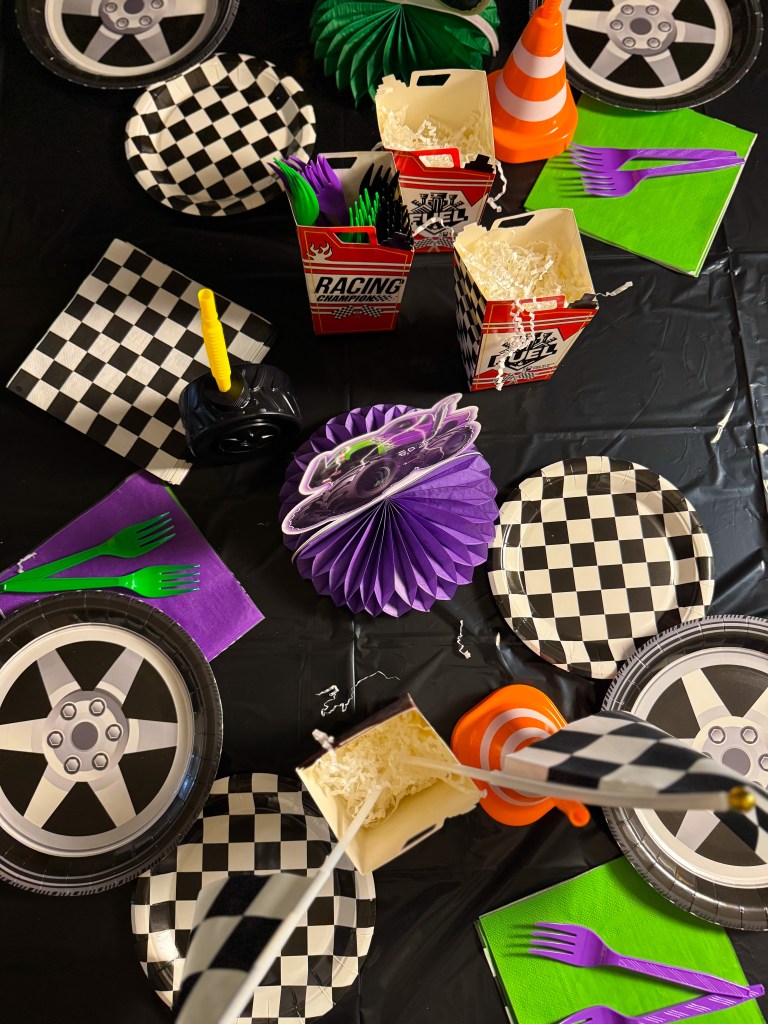 Monster truck birthday party table setup with checkered plates, racing themed decorations, traffic cone decor, and colorful party utensils.