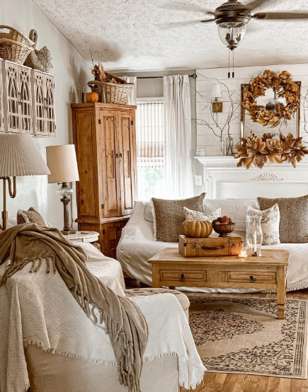 Cozy living room featuring a light-colored sofa with decorative cushions, a wooden coffee table with a pumpkin centerpiece, and warm autumn decor elements including a wreath and soft textiles.