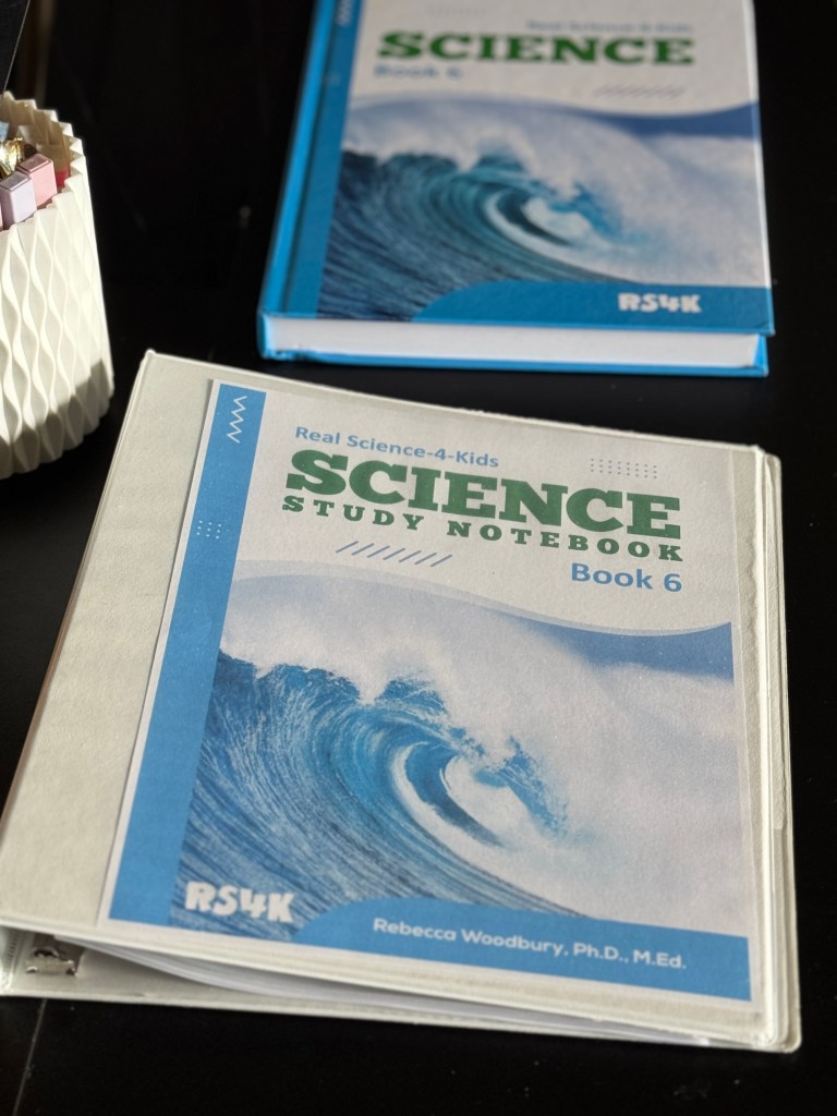 A close-up of the 'Real Science 4 Kids Book 6' textbook featuring a wave design on the cover, placed beside the 'Science Study Notebook' from the same series.