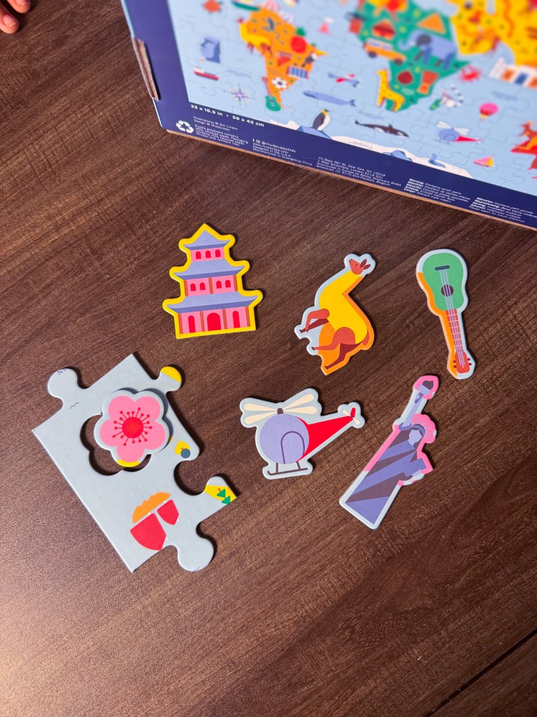 Colorful puzzle pieces featuring various shapes including a pagoda, a flamingo, a guitar, a helicopter, and a figurine, placed on a wooden surface next to a puzzle box.