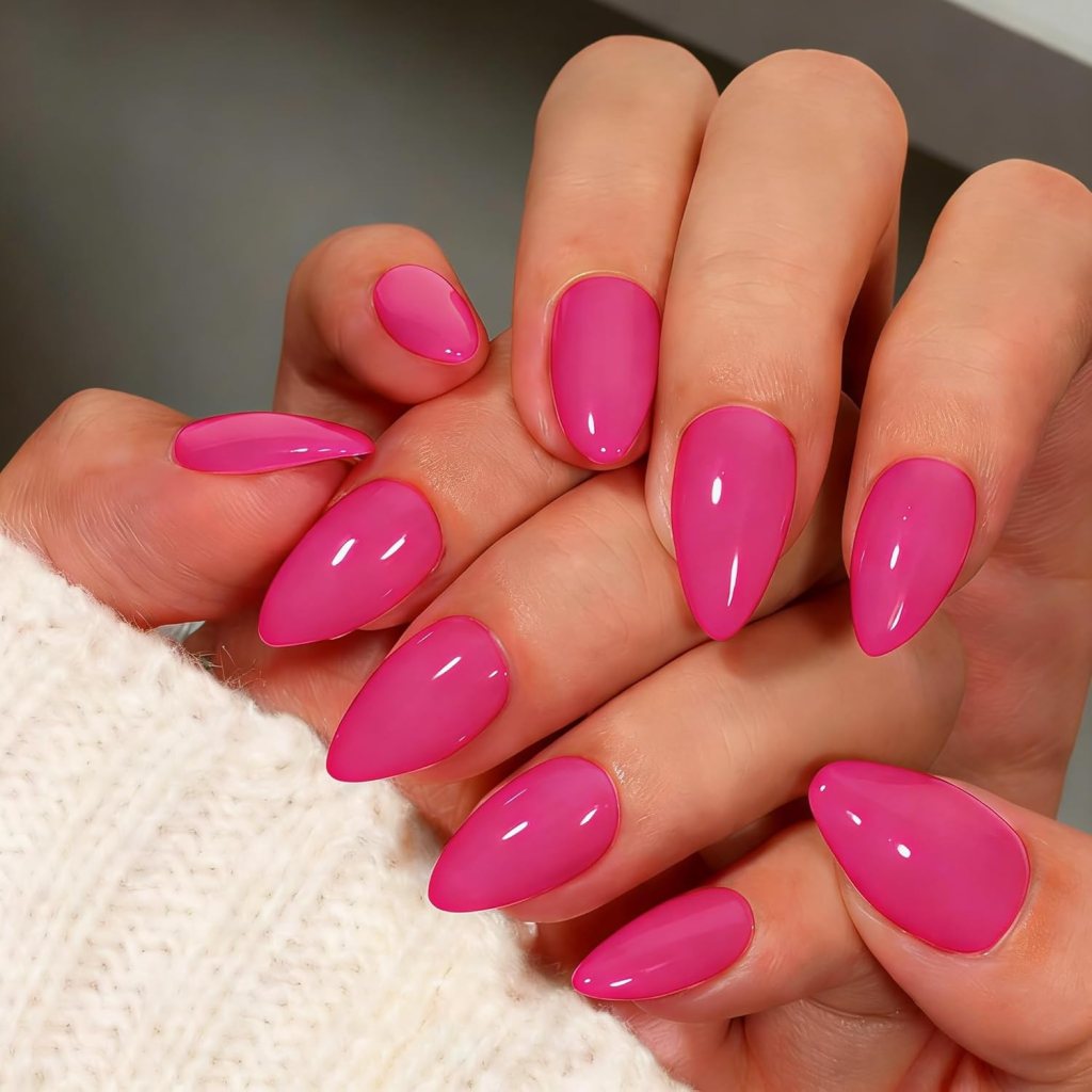 A close-up view of hands with long, pointed nails painted in a glossy pink shade, with a cozy white sweater visible in the background.