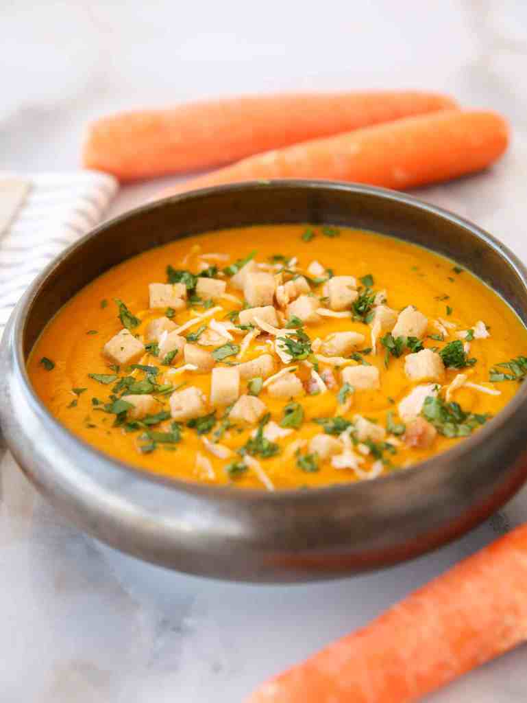 Bright orange carrot ginger soup blended smooth with coconut cream and topped with fresh herbs served in a rustic bowl