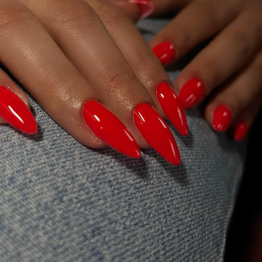 Long stiletto nails with bright red orange polish and high-shine glossy finish