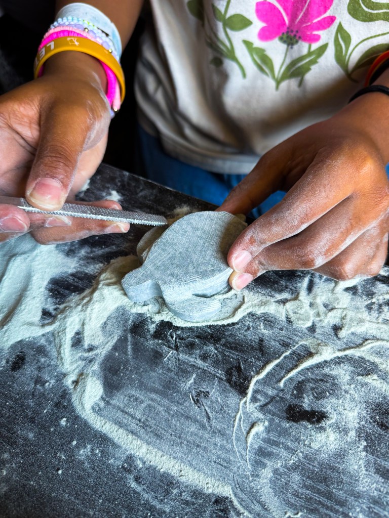 A person using a rolling pin to flatten dough on a floured surface, with their hands covered in flour.