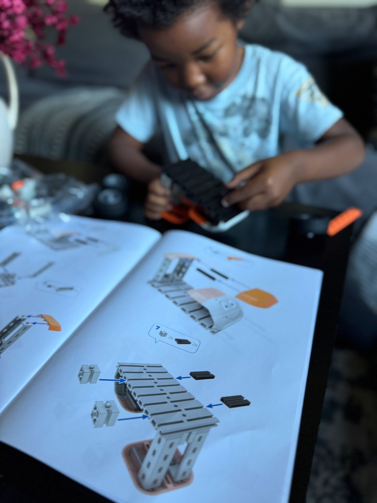A young child assembling a toy using building blocks, focused on following instructions from an open manual on a table.