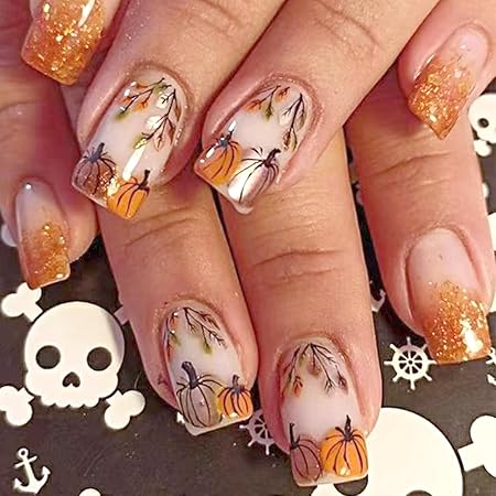 A close-up of manicured nails featuring a nude base with glittery orange tips, hand-painted autumn leaves, and small pumpkins for a festive fall look.