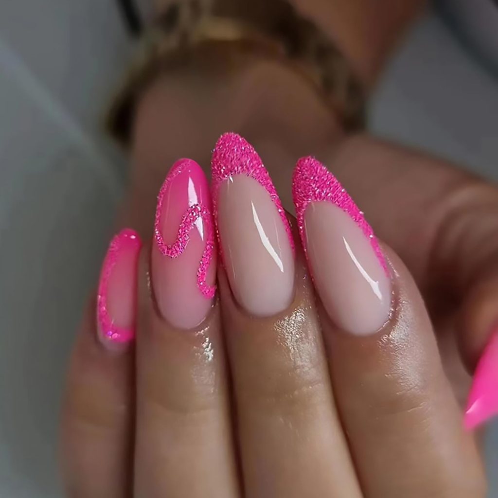 Close-up of a hand with long, almond-shaped nails featuring a pink glittery design and a natural nude base.