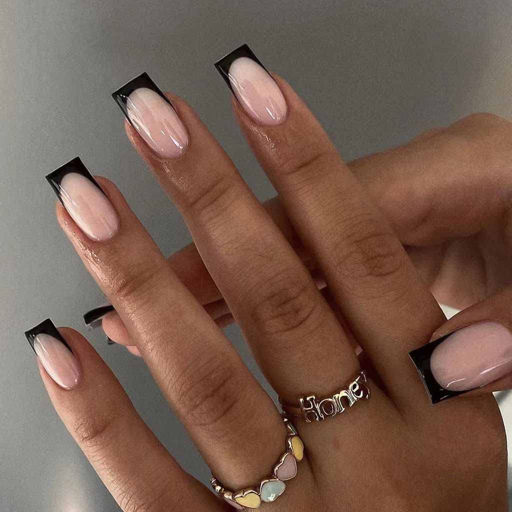 Close-up of manicured hands with long nails featuring a black tip and soft pink base, adorned with a multi-colored ring and a 'Honey' silver ring.