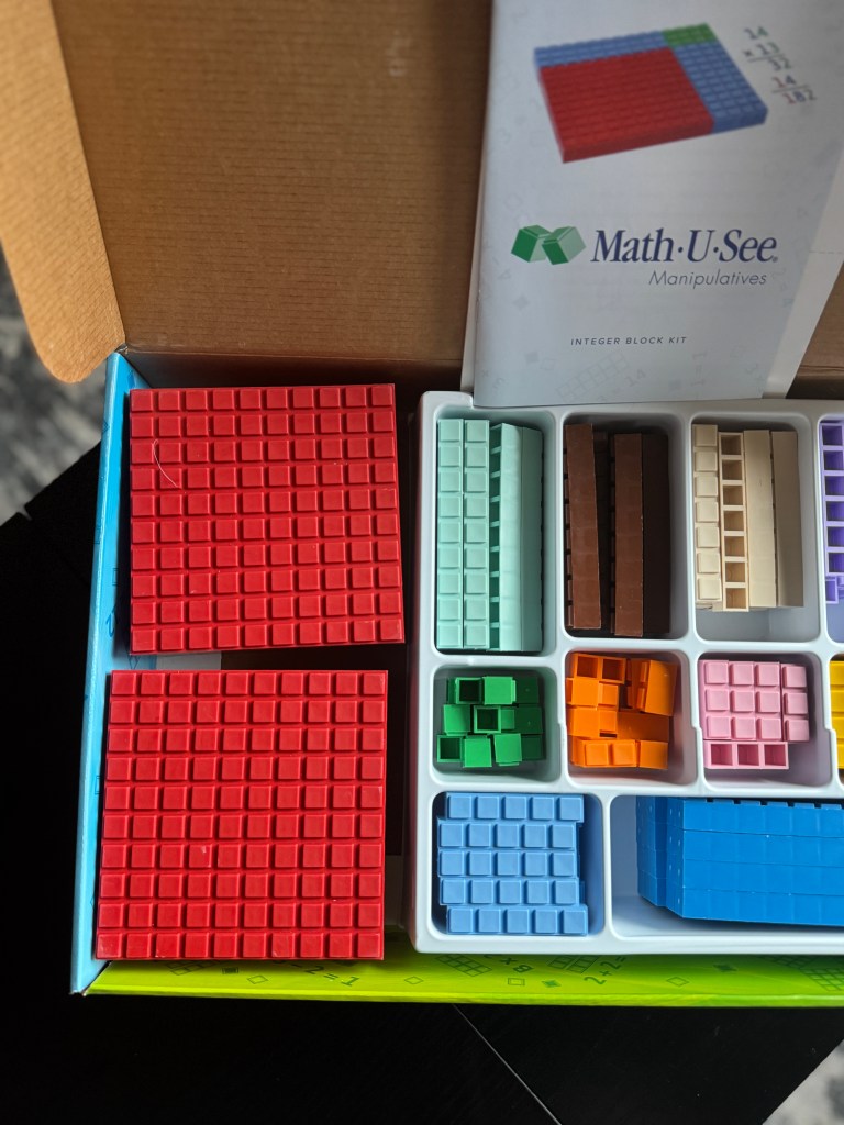Close-up view of the Math-U-See Integer Block Kit, showcasing various colored manipulatives organized in a box, including red, green, blue, and other blocks, along with the instruction booklet.