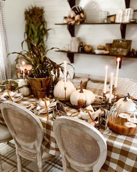 A cozy fall tablescape featuring soft white pumpkins, earthy tones, and candles, set on a light checkered tablecloth with a rustic ambiance.