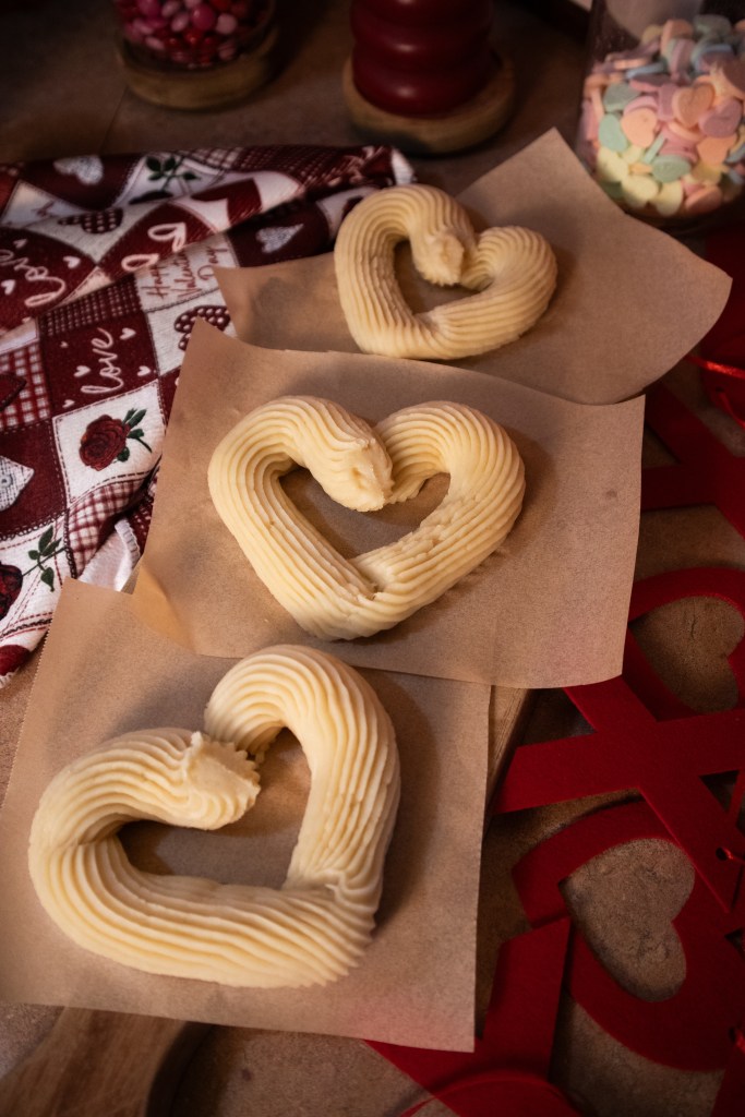 Three heart-shaped buttercream decorations on parchment paper, surrounded by a decorative cloth and red paper cutouts.