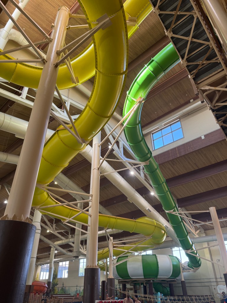 A view of the indoor water park at Great Wolf Lodge, featuring colorful water slides in yellow and green, alongside structural pillars and sunlight streaming through large windows.