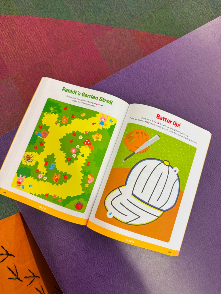 Open children's activity book featuring mazes; one page has 'Rabbit's Garden Stroll' with a colorful garden maze, and the other page has 'Batter Up!' with a baseball-themed maze.