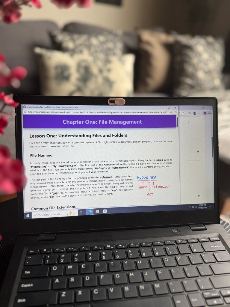 A close-up of a laptop displaying the screen of an online lesson titled 'Chapter One: File Management,' outlining file naming conventions with examples and definitions related to files and folders.