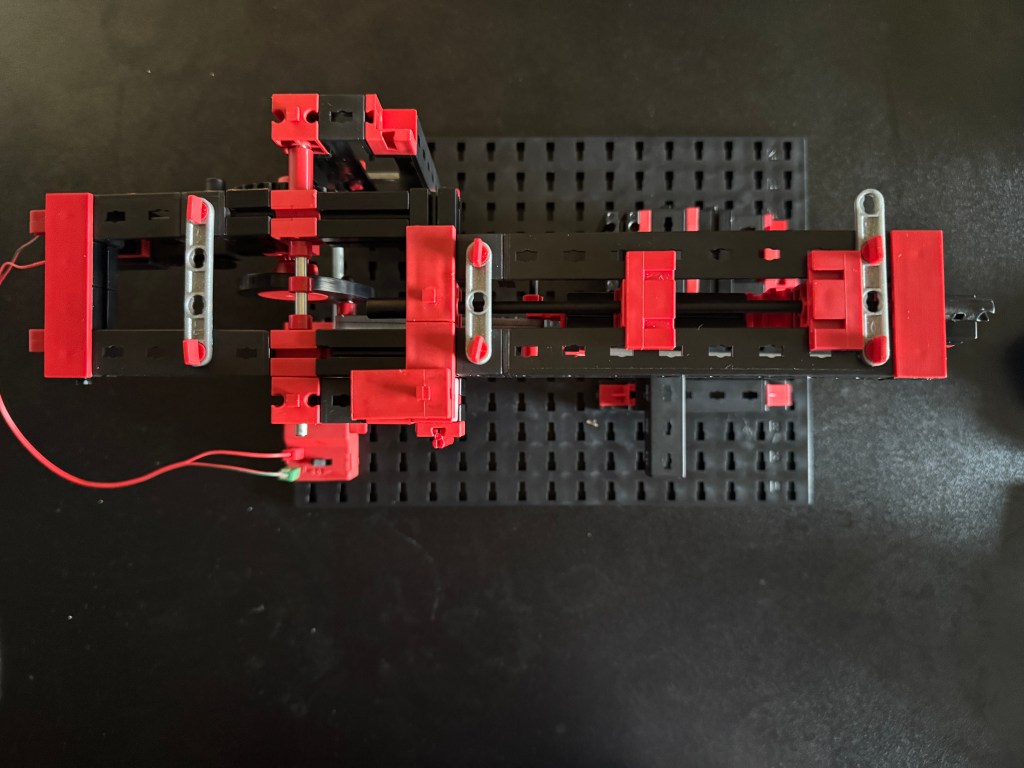 Aerial view of a Fischer Technik STEM kit assembly with red and black components on a black base plate.