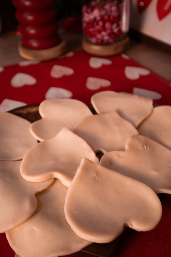 Heart-shaped pieces of dough arranged on a wooden platter, set on a red heart-patterned tablecloth.