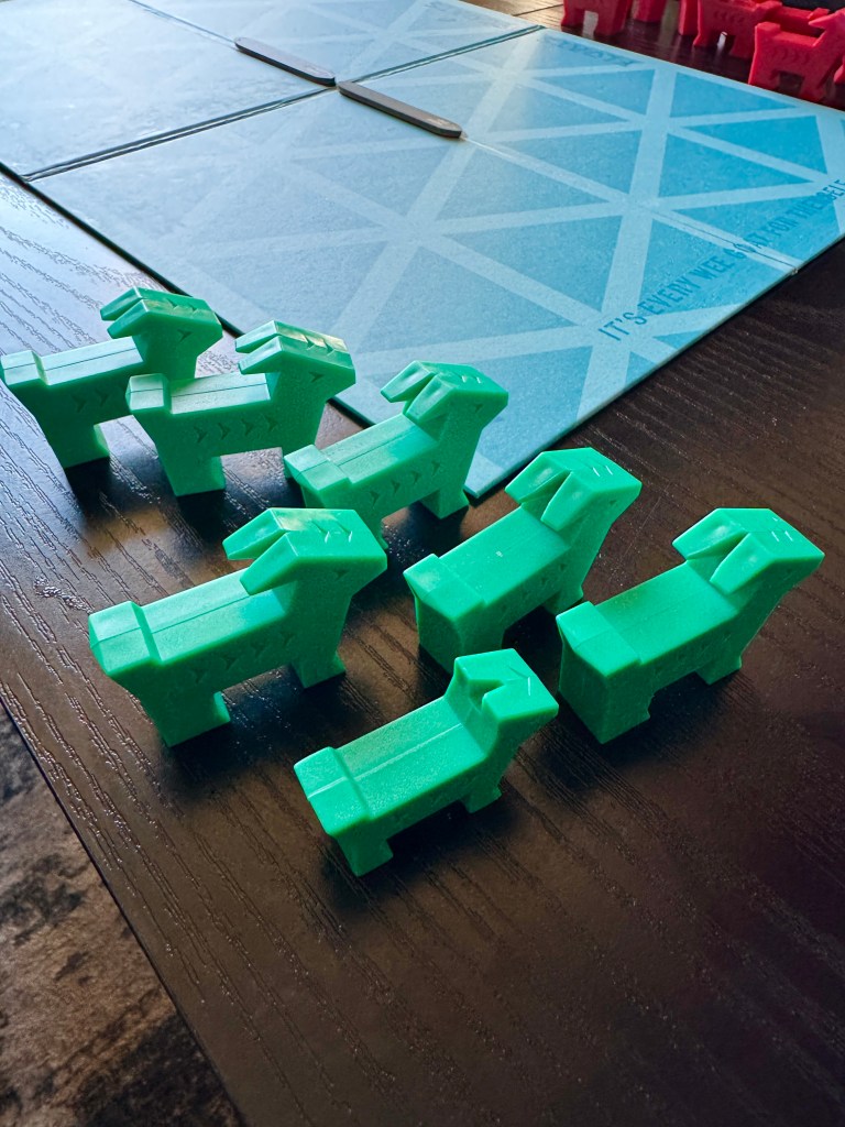 A collection of green plastic animal figures resembling dogs, arranged on a wooden table next to a light blue patterned board game.