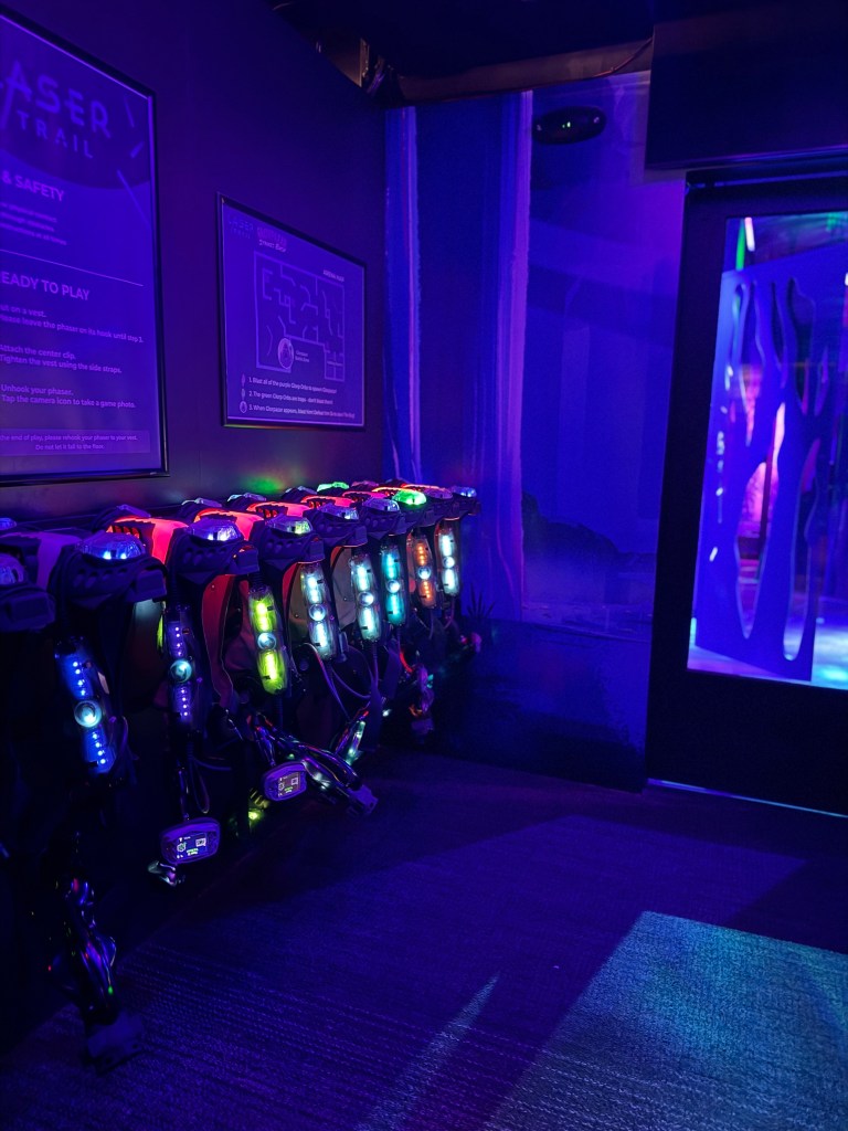 A darkened laser tag arena with glowing laser tag vests ready for players, set against a purple and blue backdrop.