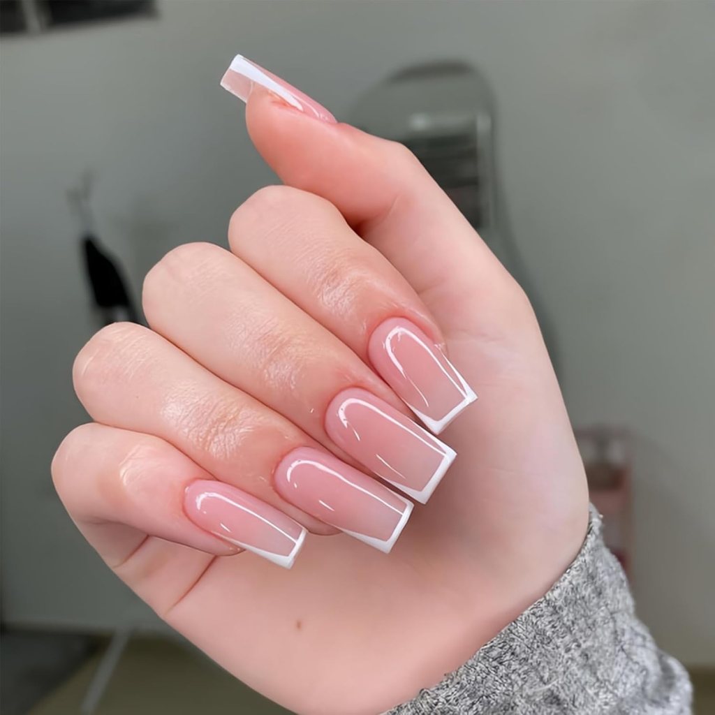 A hand displaying well-manicured long nails with a glossy nude base and white tips.