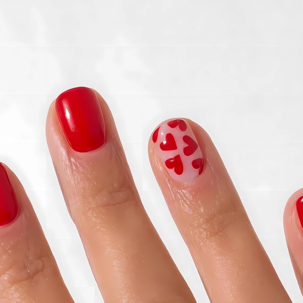 Close-up of manicured fingers with three red nails and one white nail decorated with small red hearts.