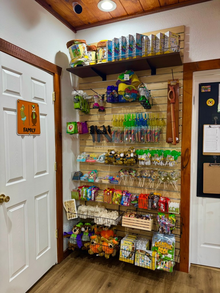 A colorful display of various snacks, toys, and craft items arranged on shelves against a wall, with a white door on the left side and a family-themed sign.