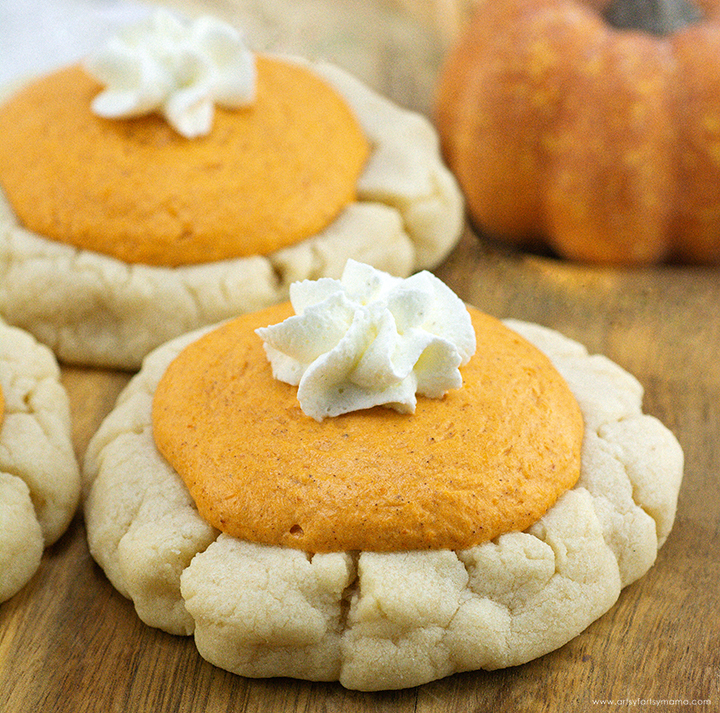 Two pumpkin cookie truffles topped with whipped cream on a wooden surface, with a small pumpkin in the background.