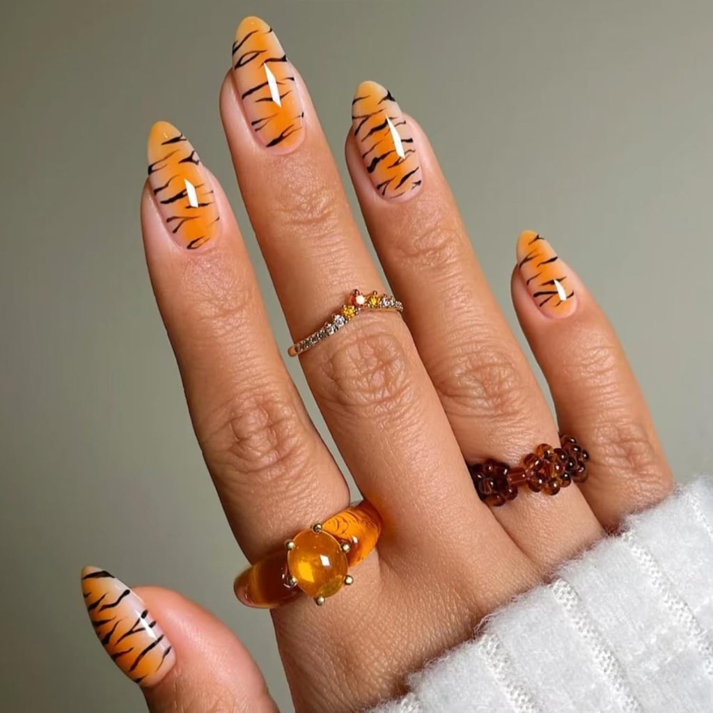 Almond-shaped orange nails with black tiger stripe design on a sheer nude base