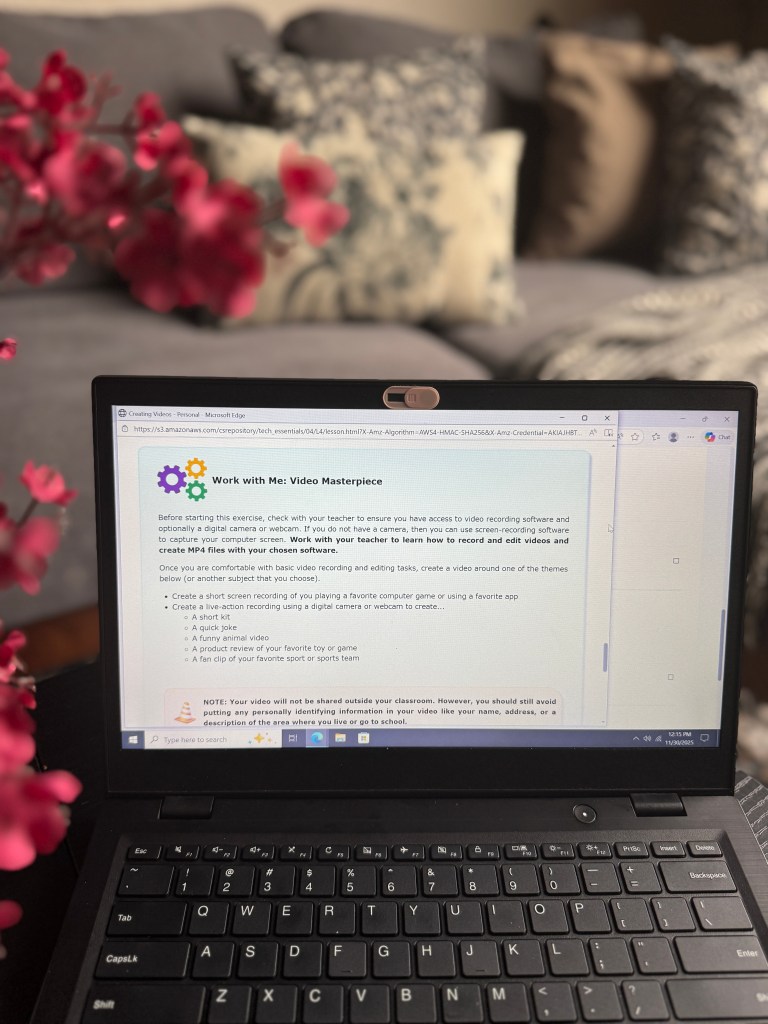 A laptop displaying a lesson on video creation techniques for a digital curriculum, with floral elements in the foreground and a cozy living room background.