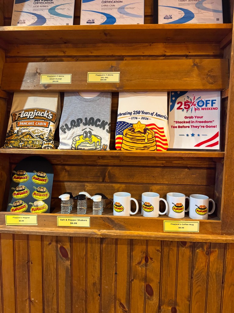 Flapjack's Pancake Cabin souvenir display featuring branded T-shirts, coffee mugs, magnets, and other gifts.