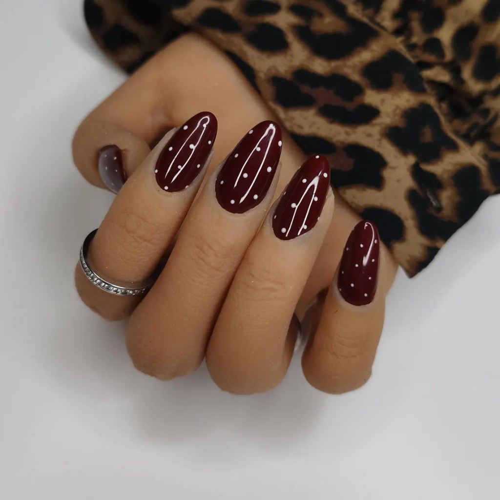 Close-up of a hand with elegant burgundy nails featuring white polka dots, resting over a leopard print fabric.