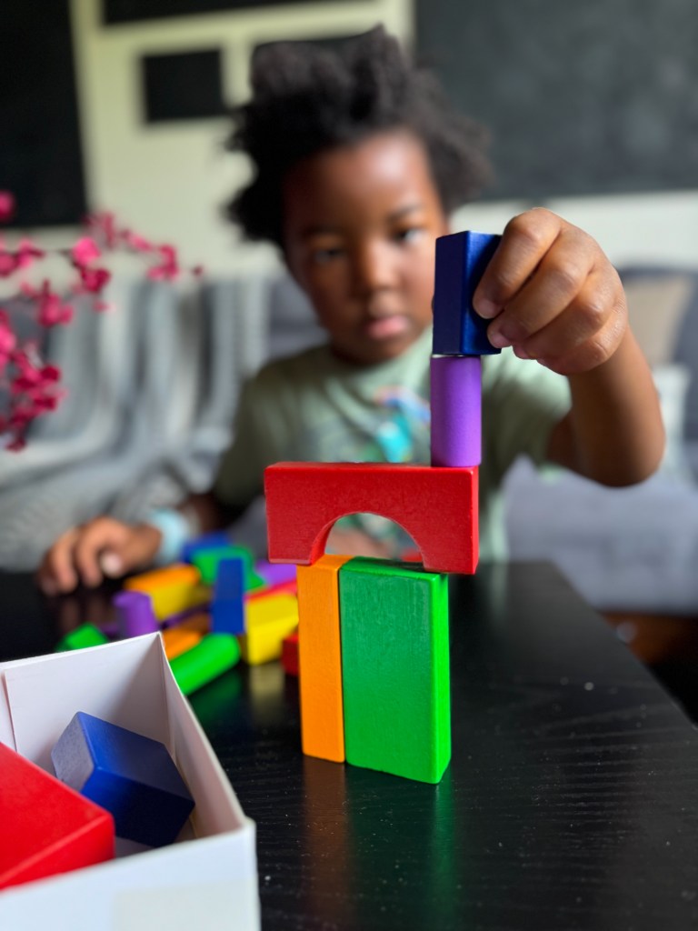 A child building a colorful structure with various geometric blocks on a table.