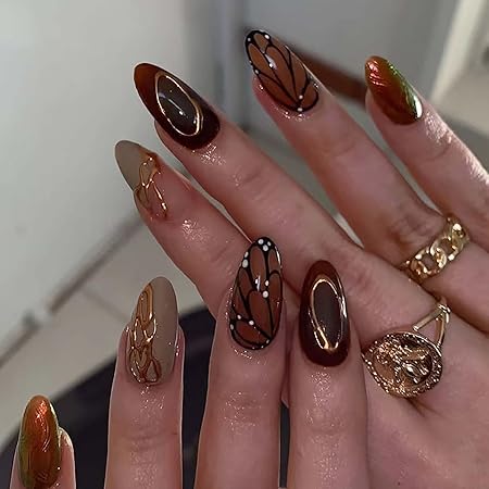 A close-up of hands with stylish autumn-themed nail art featuring brown, caramel, and nude colors with intricate designs inspired by butterfly wings.