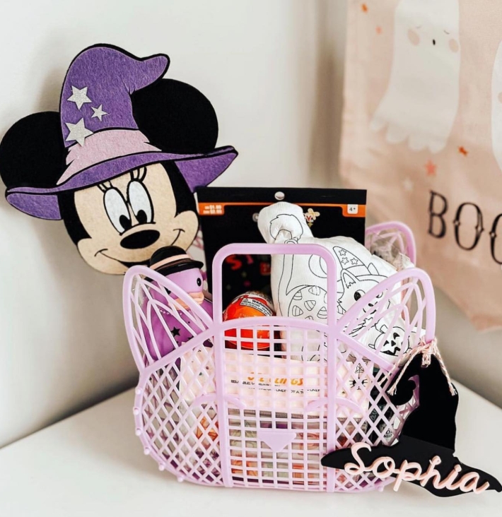 A pastel purple mini basket filled with Halloween treats, plush toys, and a felt Minnie Mouse wearing a witch hat, personalized with a name tag.