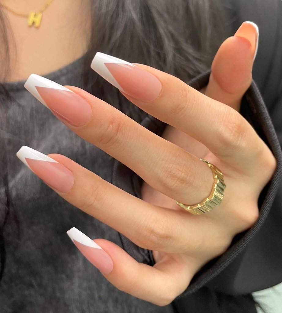 Close-up of a hand with elegantly manicured long nails featuring a nude base and white tips, adorned with a gold ring.